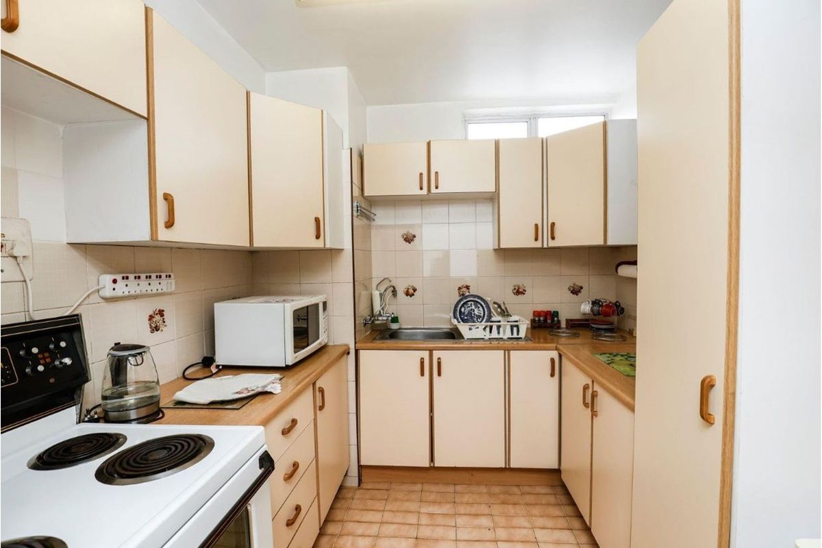 A compact, dated kitchen featuring laminate cabinetry, tiled splashbacks, and a functional electric stove, offering potential for a modern renovation.