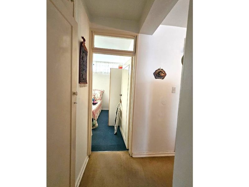 A view through a hallway leading into a bedroom, featuring carpeted flooring and a transom window above the doorway.