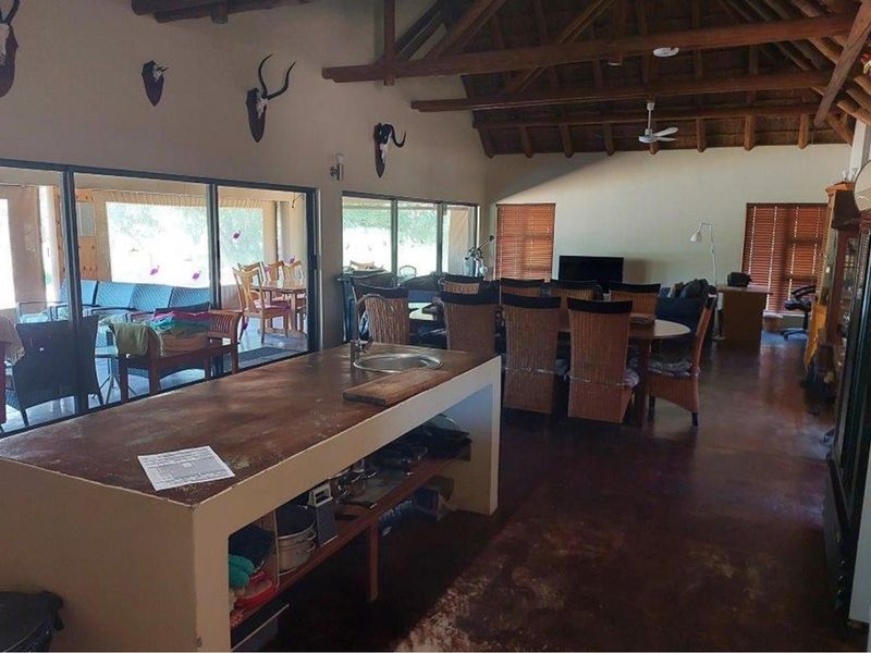 Spacious open-plan living and dining area featuring a large kitchen island, exposed timber roof trusses, and expansive sliding glass doors leading to the patio.