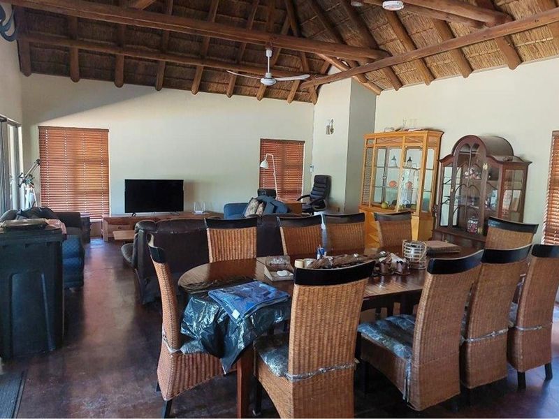 Spacious open-plan living and dining area featuring a high vaulted thatched ceiling with exposed timber beams and polished concrete flooring.