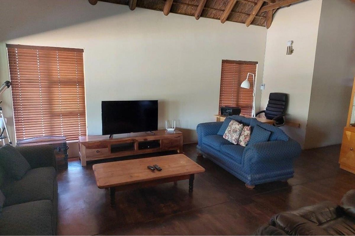 Spacious living room featuring high vaulted thatched ceilings, dark polished concrete flooring, and large windows with fitted wooden blinds.