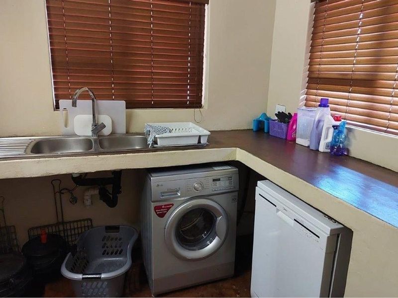 Functional laundry area featuring a double stainless steel sink, built-in concrete countertop, and dedicated space for laundry appliances.