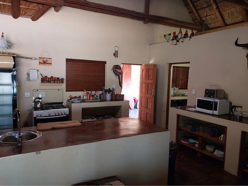 Rustic kitchen featuring a thatched roof, built-in masonry cabinetry, a central island with a sink, and a freestanding gas stove.