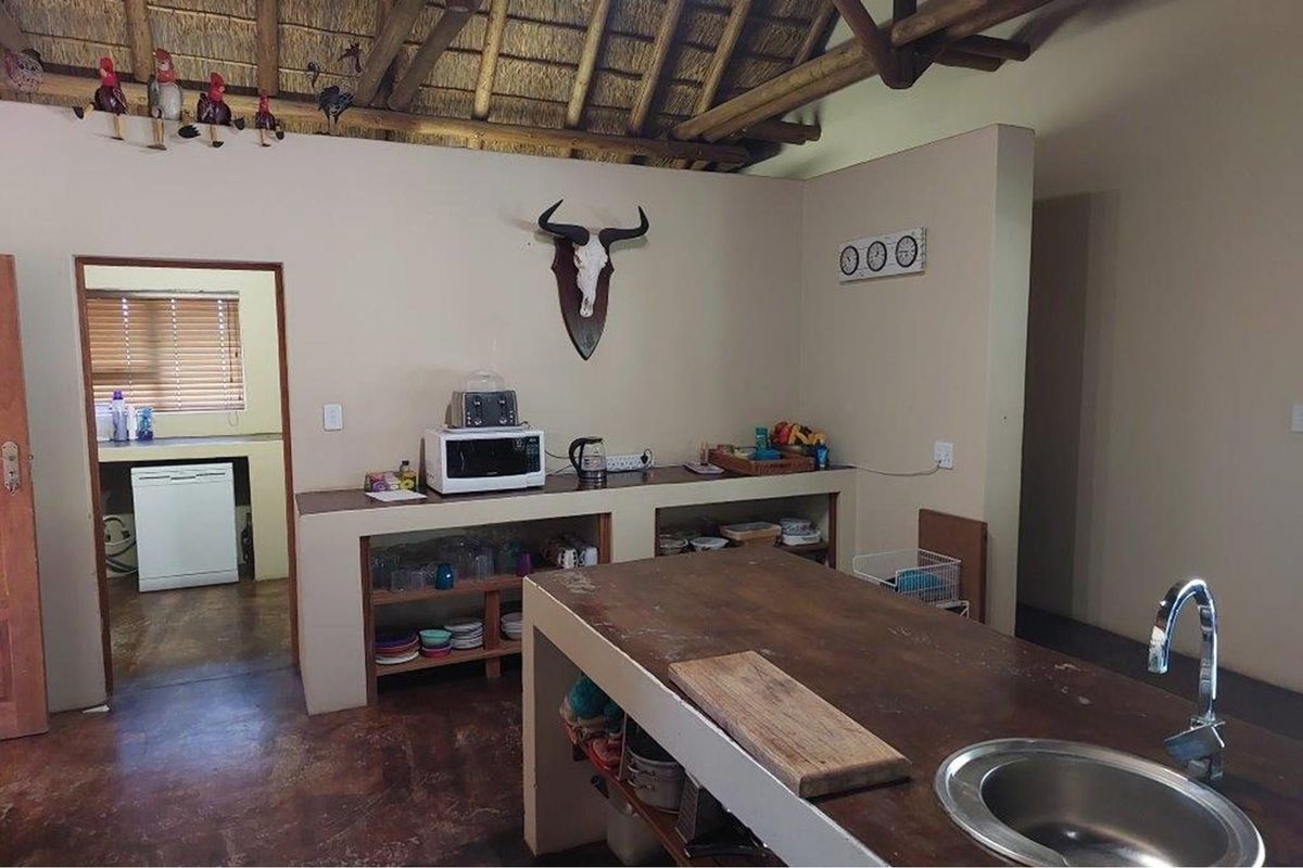 Rustic kitchen featuring a thatched roof, built-in concrete cabinetry, a central island with a sink, and an adjacent scullery area.