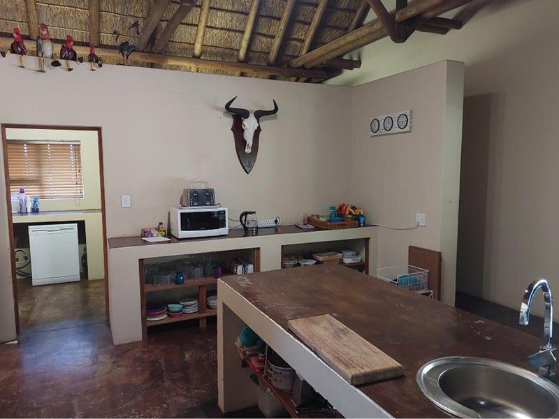 Rustic kitchen featuring a thatched roof, built-in concrete cabinetry, a central island with a sink, and an adjacent scullery area.