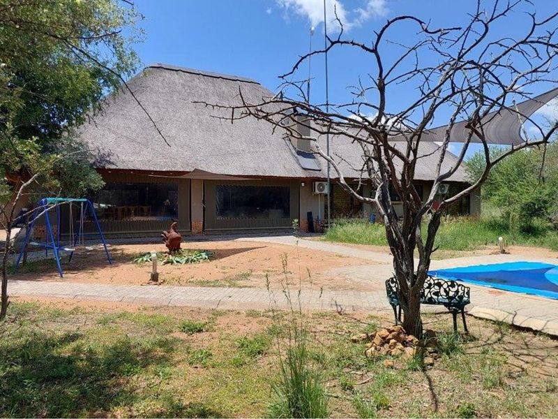 Rear view of a thatched roof house featuring a swimming pool, paved patio area, and established garden surroundings.
