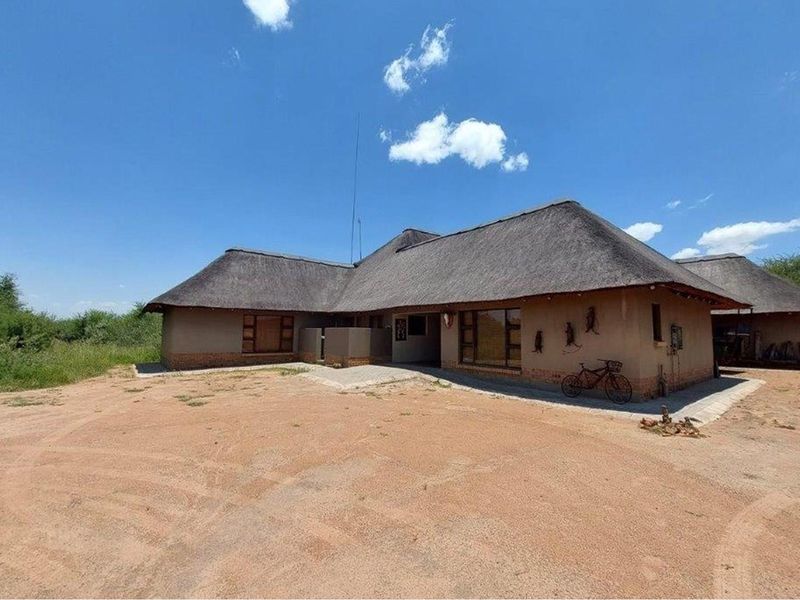 A single-story house featuring a traditional thatched roof and earth-toned exterior walls, set within a natural, open landscape.