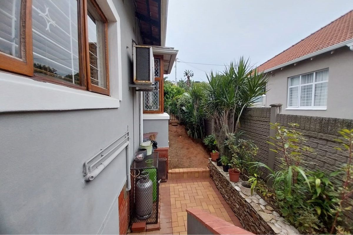A side exterior walkway featuring paved flooring, a retaining wall with garden beds, and an external air conditioning unit.