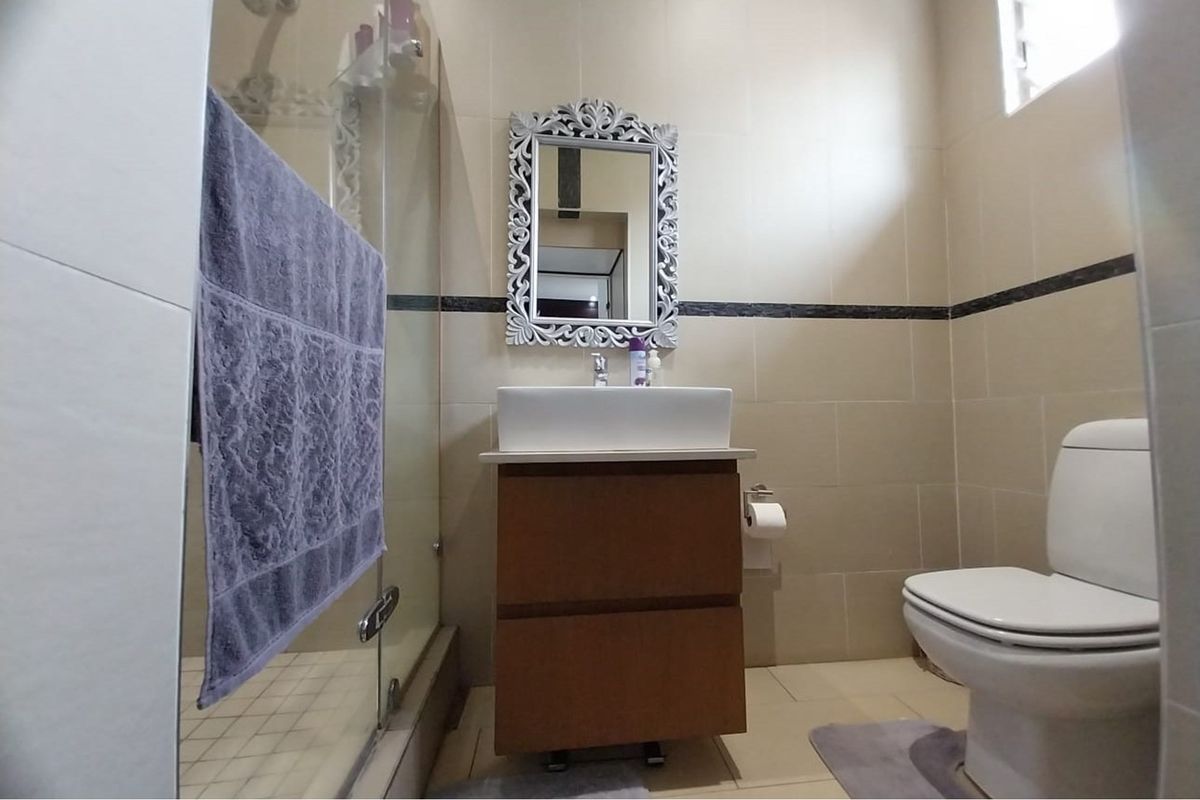 A modern bathroom featuring a vessel sink vanity, a glass-enclosed shower, and neutral wall tiling with a decorative border.