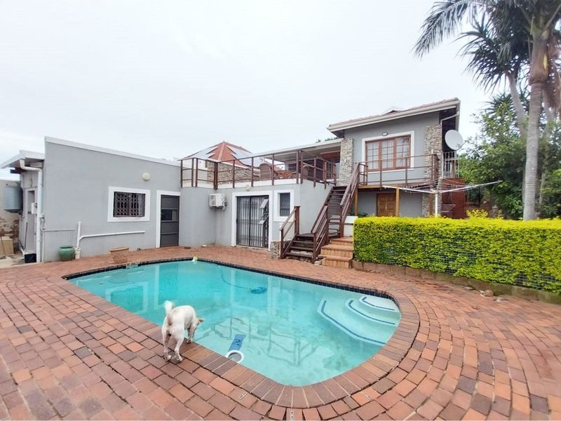 Rear exterior view featuring a swimming pool, brick paved patio area, and an elevated wooden deck accessible via an external staircase.