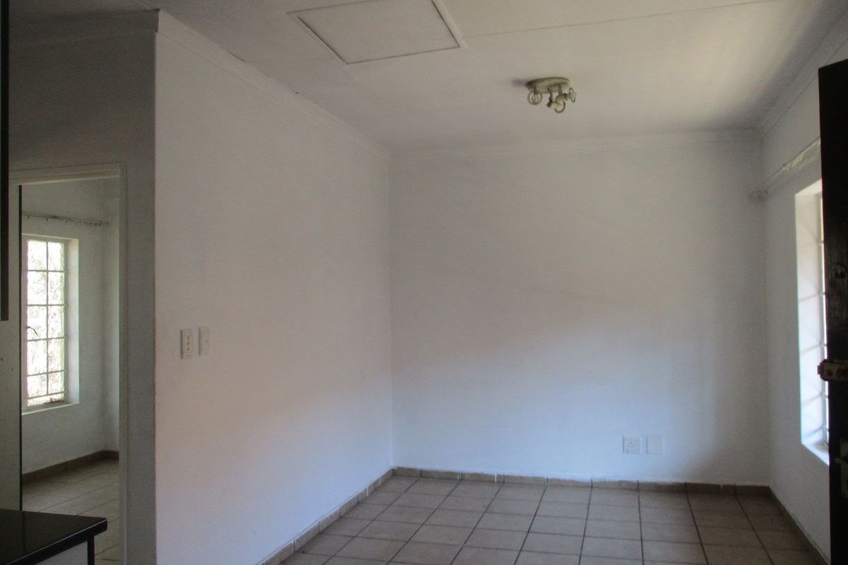 An empty living area featuring tiled flooring, neutral walls, and a view into an adjacent room through a doorway.
