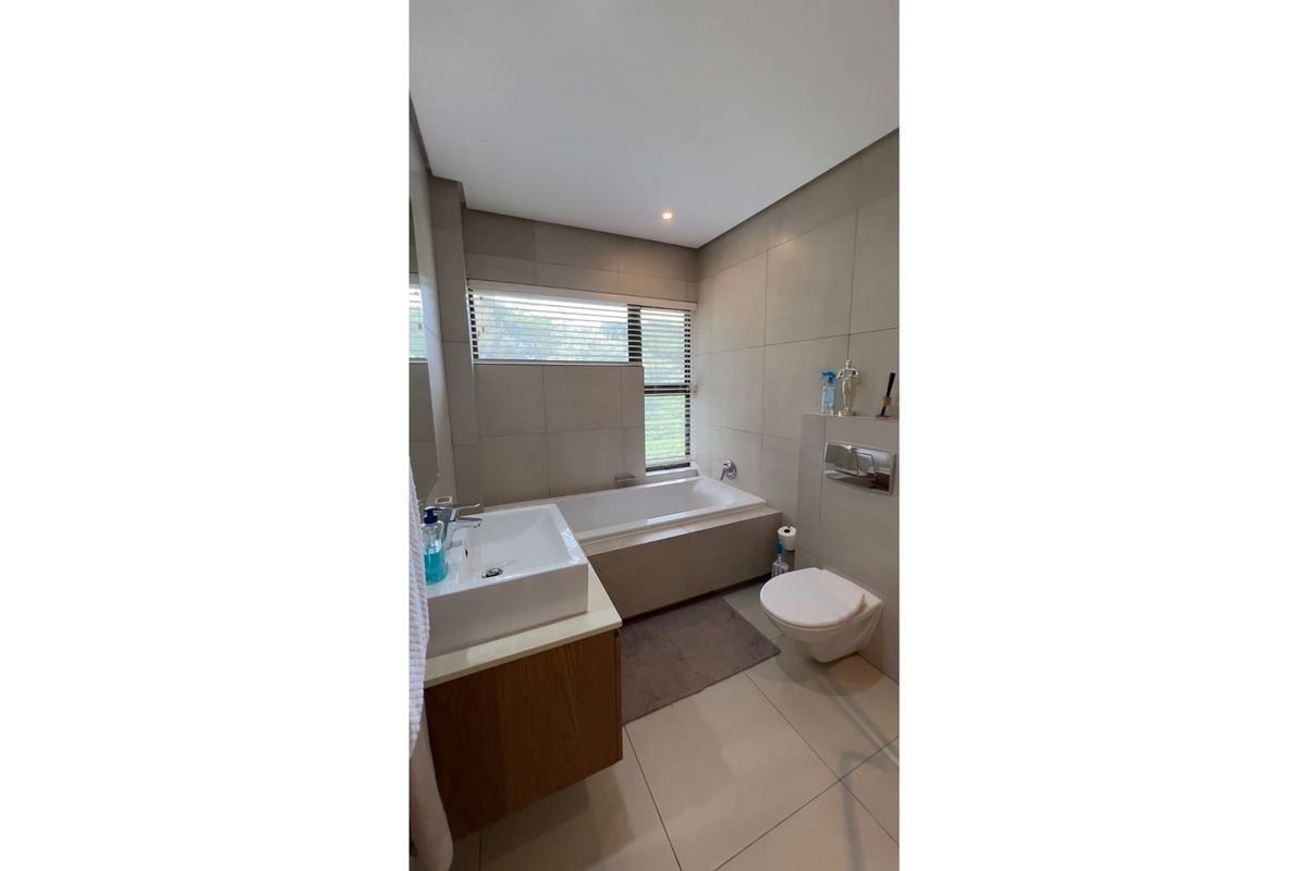 Modern bathroom featuring a built-in bathtub, wall-mounted toilet, and a vanity with a basin, finished with neutral floor-to-ceiling tiles.