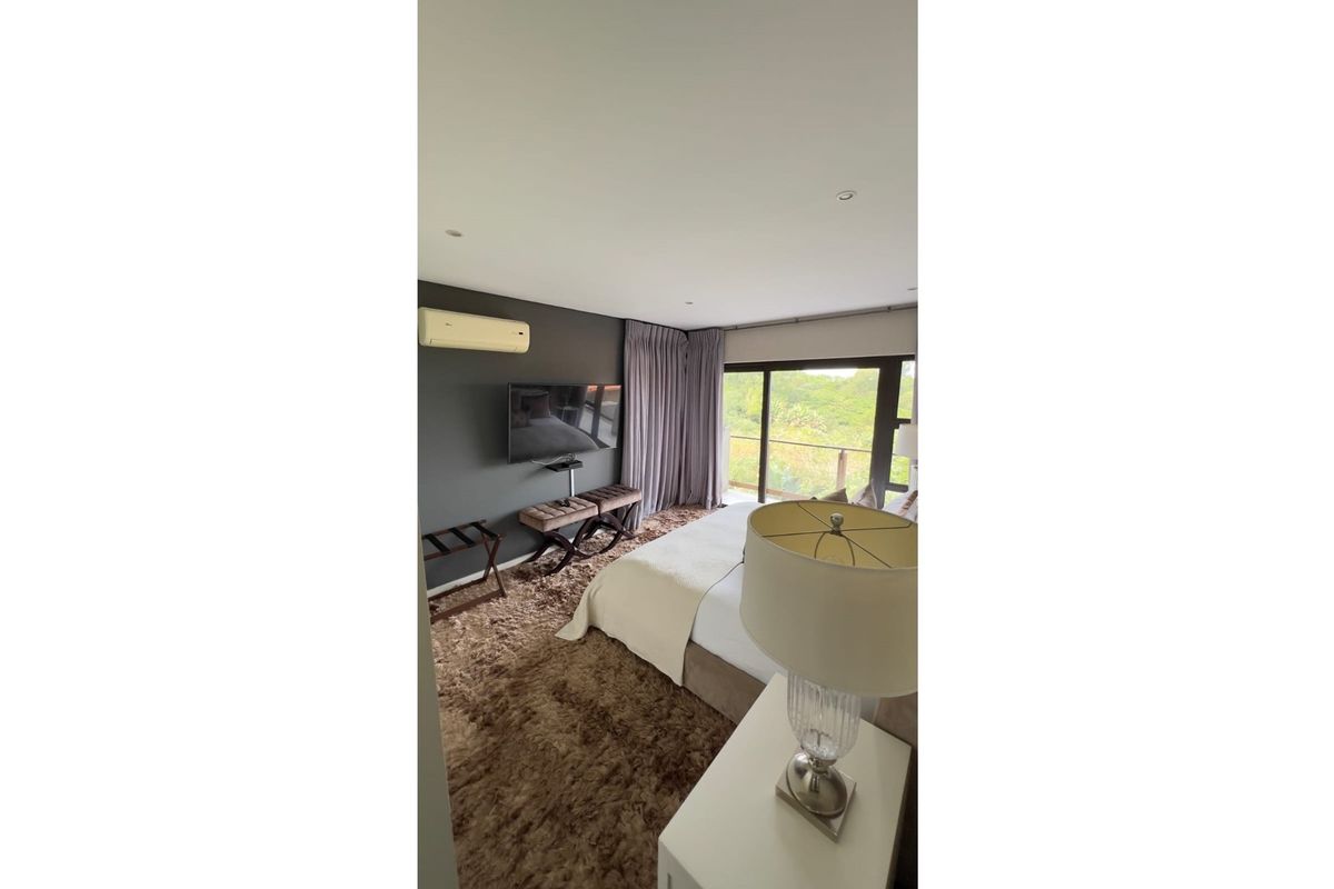 A well-appointed bedroom featuring a wall-mounted air conditioning unit, large sliding glass doors leading to a balcony, and recessed ceiling lighting.