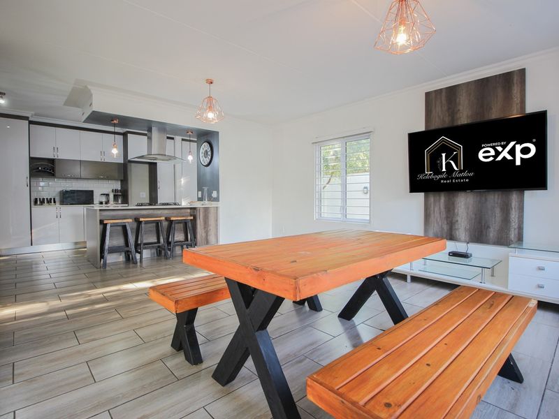 Modern open-plan living area featuring a contemporary kitchen with island, tiled flooring, and a stylish feature wall with integrated television mount.