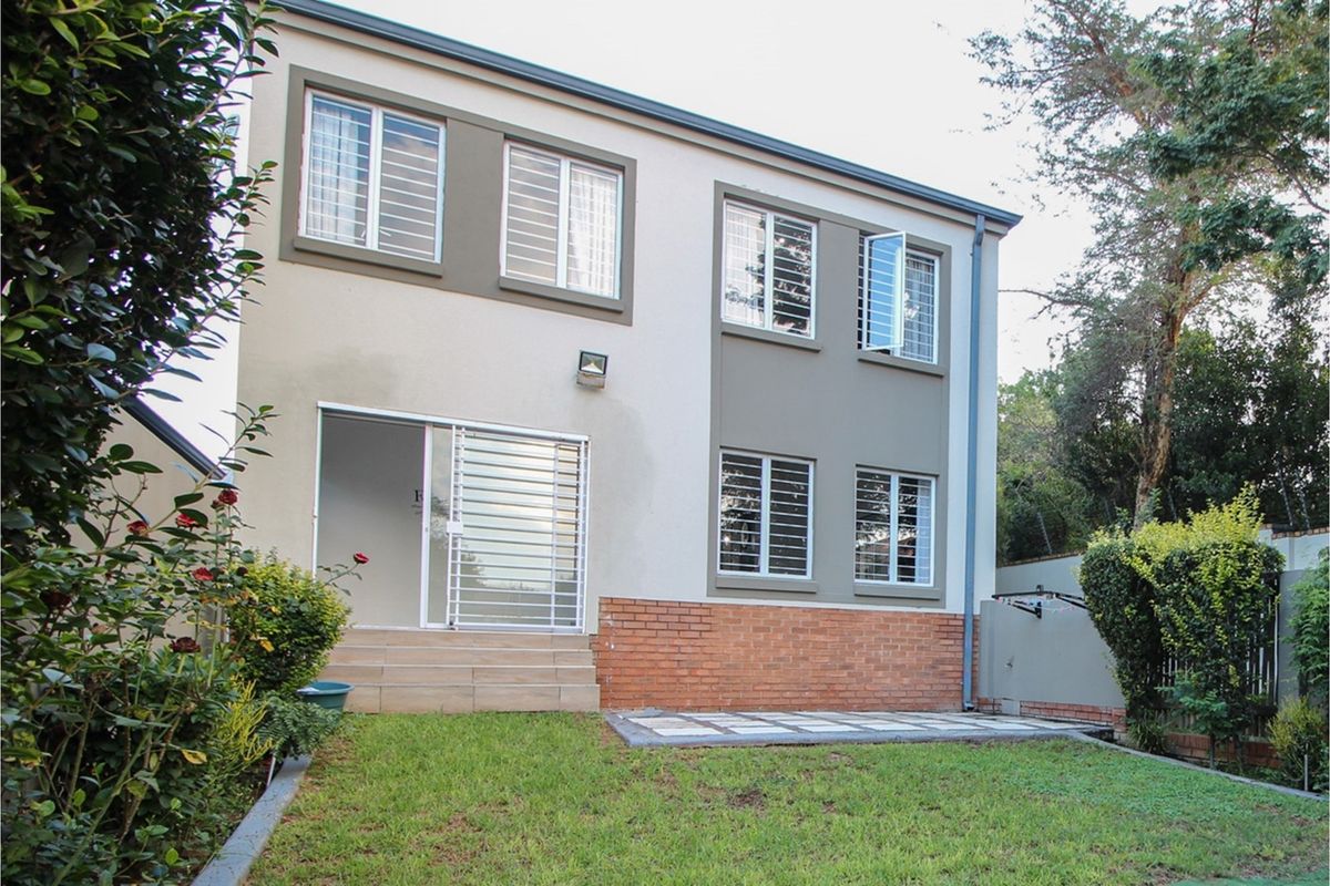 Rear view of a two-story residential property featuring a brick and plaster facade, security bars on windows, and a small paved patio area.