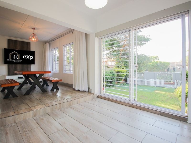 A bright living area featuring tiled flooring, a raised floor section, and large sliding glass doors with security bars overlooking the garden.