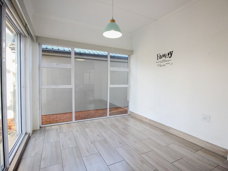 A bright, empty living area featuring modern wood-look floor tiles, large glass sliding doors providing natural light, and a contemporary pendant light fixture.