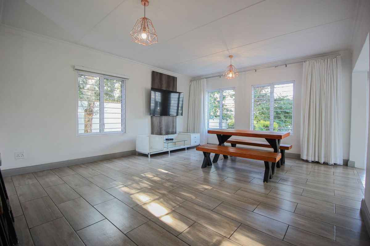Bright and spacious living area featuring modern tiled flooring, large windows with security bars, and a built-in TV wall panel.