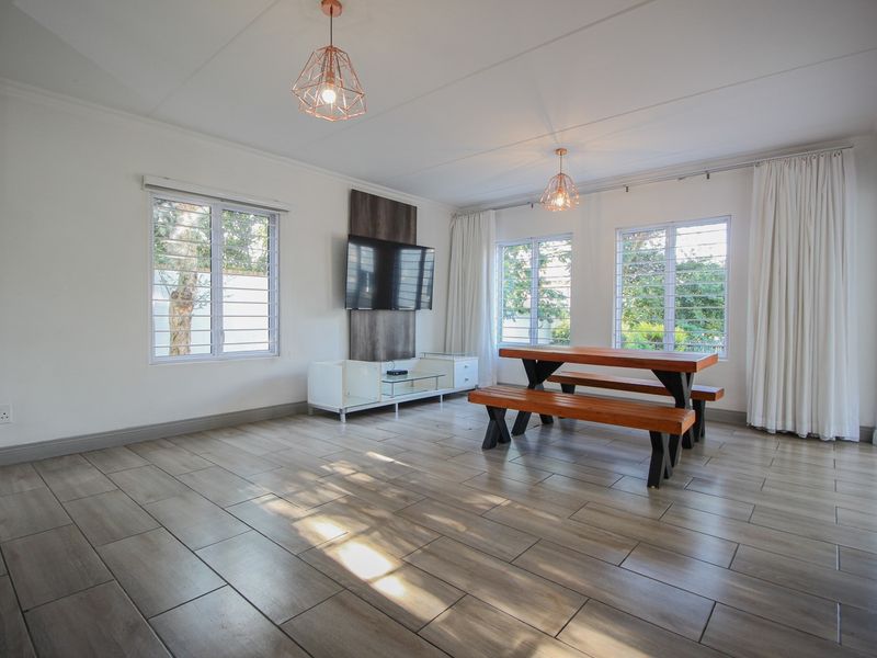 Bright and spacious living area featuring modern tiled flooring, large windows with security bars, and a built-in TV wall panel.