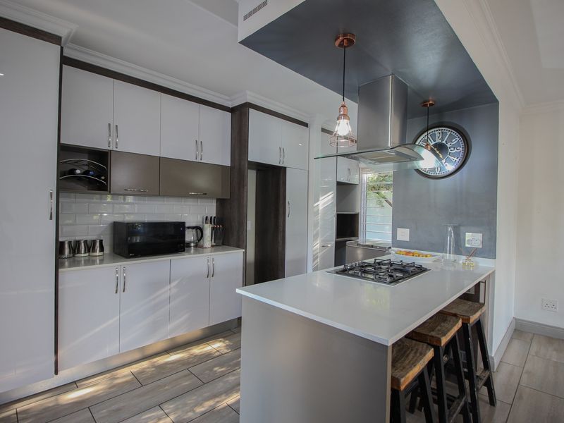 Modern kitchen featuring sleek white and dark cabinetry, stone countertops, a central island with a gas hob, and stylish pendant lighting.