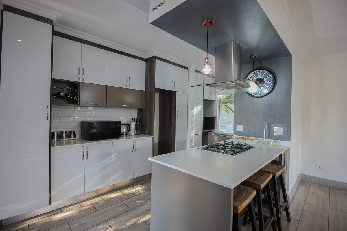 Modern kitchen featuring sleek white and dark cabinetry, stone countertops, a central island with a gas hob, and stylish pendant lighting.