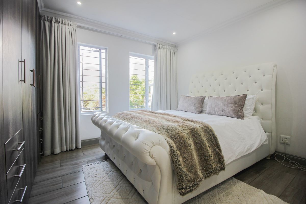 A well-maintained bedroom featuring laminate flooring, built-in cupboards, recessed downlighting, and large windows with security bars.