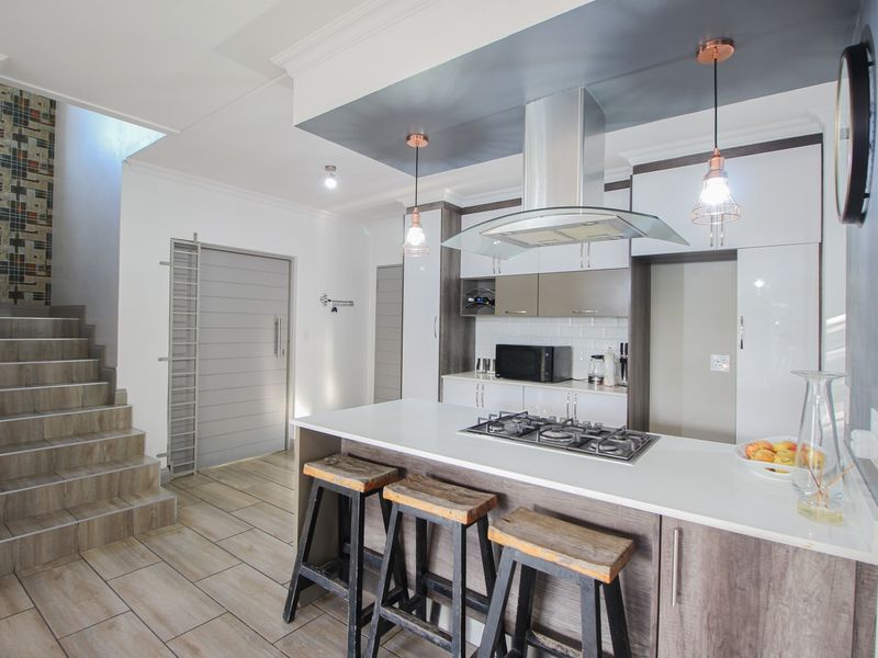 Modern open-plan kitchen featuring a central island with gas hob, sleek cabinetry, tiled flooring, and an adjacent staircase with decorative tiling.