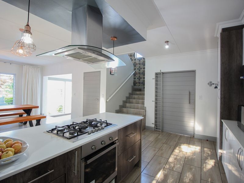 Modern open-plan kitchen featuring a central island with gas hob, built-in oven, extractor fan, and tiled flooring, seamlessly connecting to the living and staircase area.