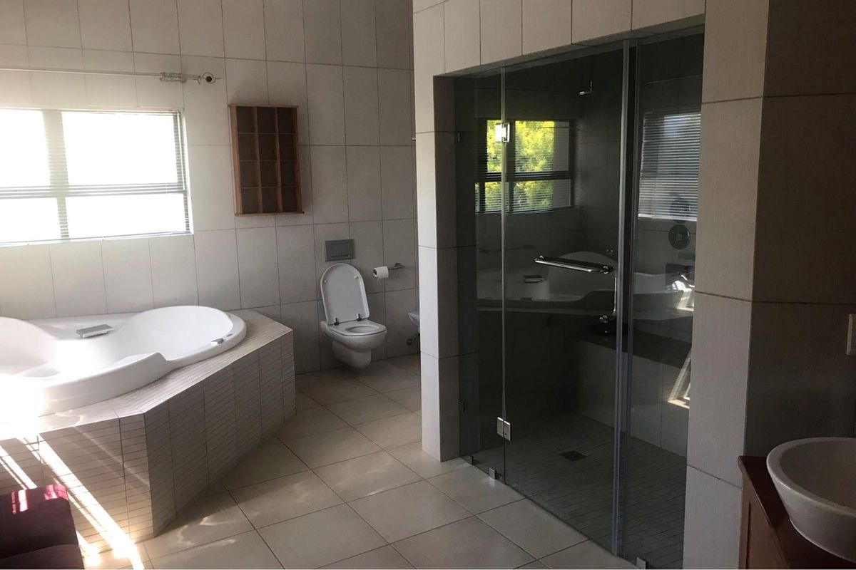Spacious bathroom featuring a built-in corner bathtub, a wall-mounted toilet, and a modern glass-enclosed shower with neutral tiled finishes throughout.