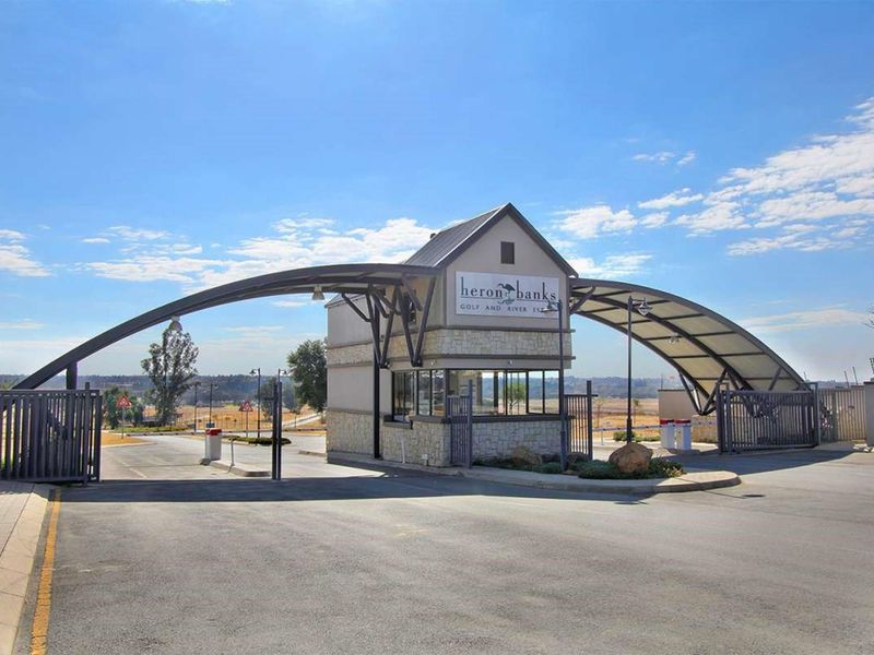 The main entrance gatehouse of Heron Banks Golf and River Estate, featuring a modern arched structure, security booth, and paved access road.