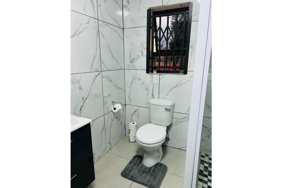 Modern bathroom featuring marble-look wall tiles, a sleek vanity, and a secure window with burglar bars.
