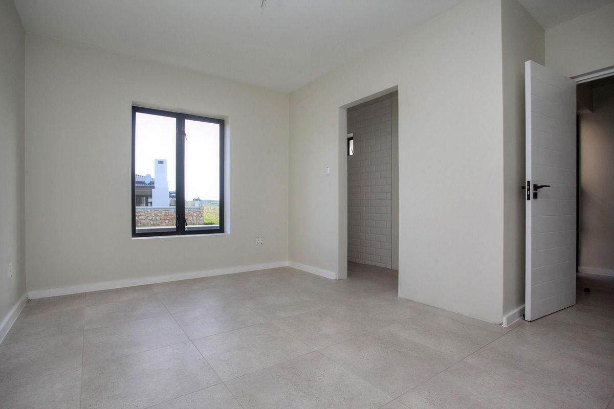 A bright, modern, and empty bedroom featuring neutral tiled flooring, clean white walls, and a doorway leading to an adjacent space.