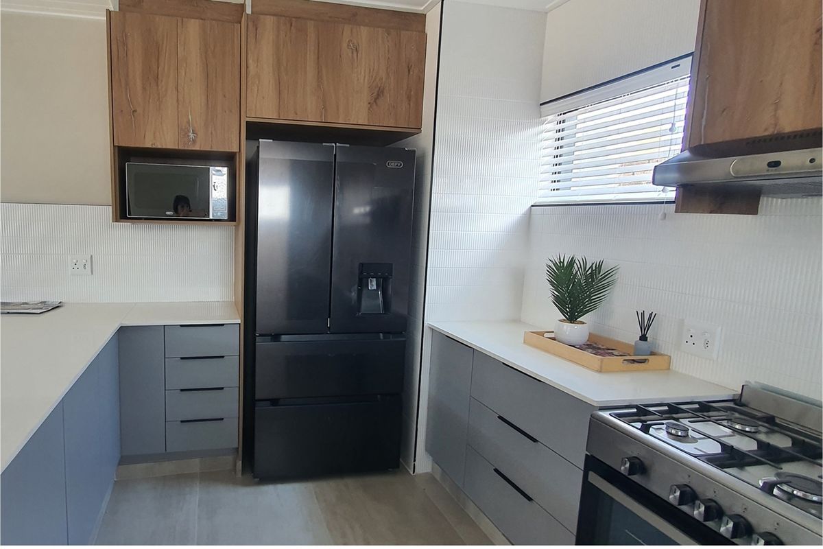 Modern kitchen featuring wood-grain upper cabinetry, grey lower cabinets, white stone countertops, and integrated stainless steel gas stove and extractor fan.
