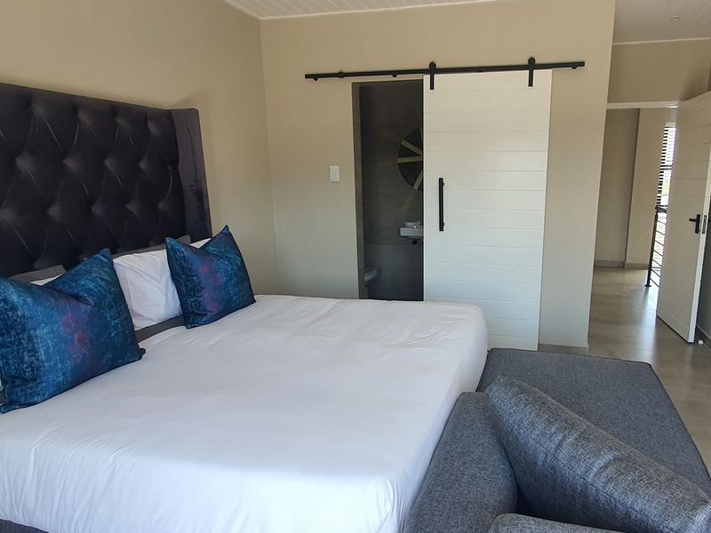 A well-maintained bedroom featuring a modern sliding barn door leading to an en-suite bathroom, with neutral wall tones and tiled flooring.