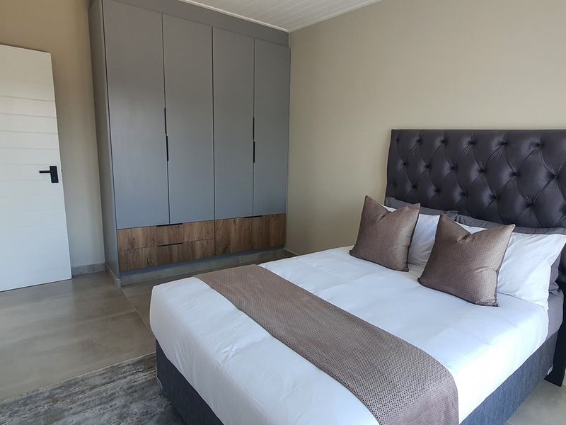 A modern bedroom featuring built-in grey and wood-tone cabinetry, neutral wall finishes, and tiled flooring.