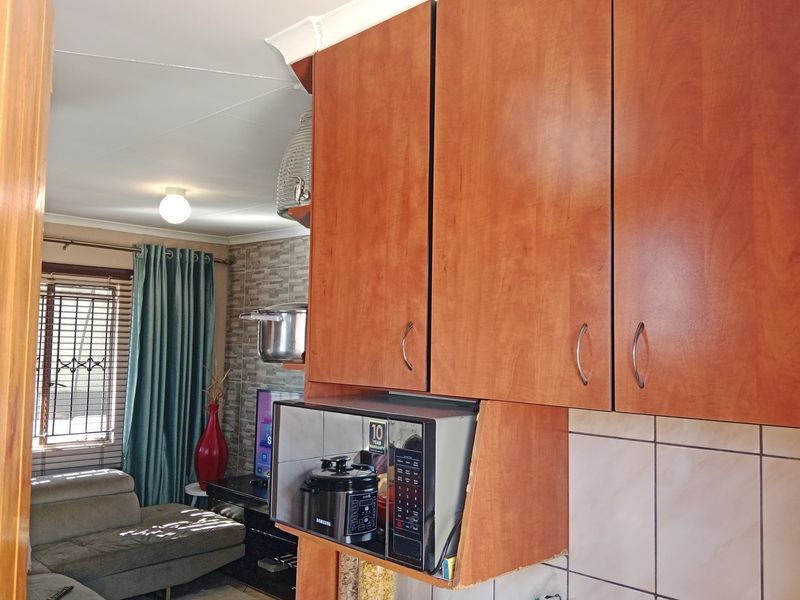 Open plan living area featuring wooden cabinetry with integrated microwave space and tiled backsplash, connecting to a lounge area with security window bars.