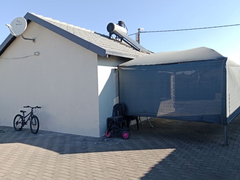 Rear exterior view of the property featuring a paved driveway, solar water heating system, and a temporary shade cloth structure.