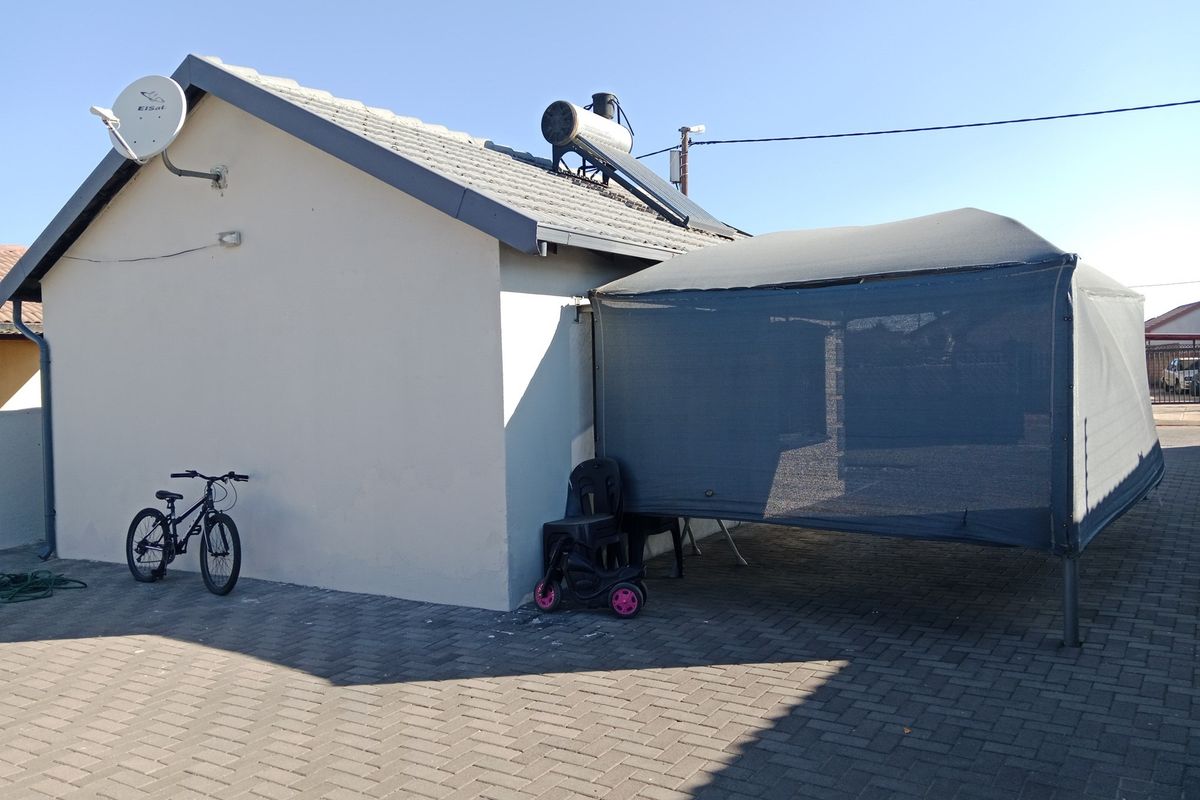Rear exterior view of the property featuring a paved driveway, solar water heating system, and a temporary shade cloth structure.