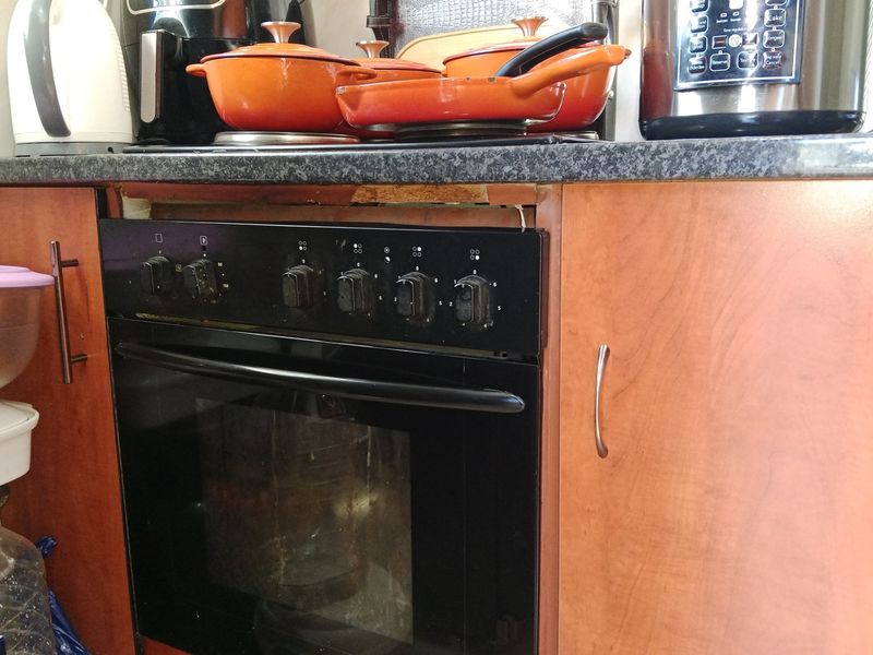 Close-up view of a kitchen oven unit featuring wood-look cabinetry and a granite countertop, showing a missing trim panel above the oven.
