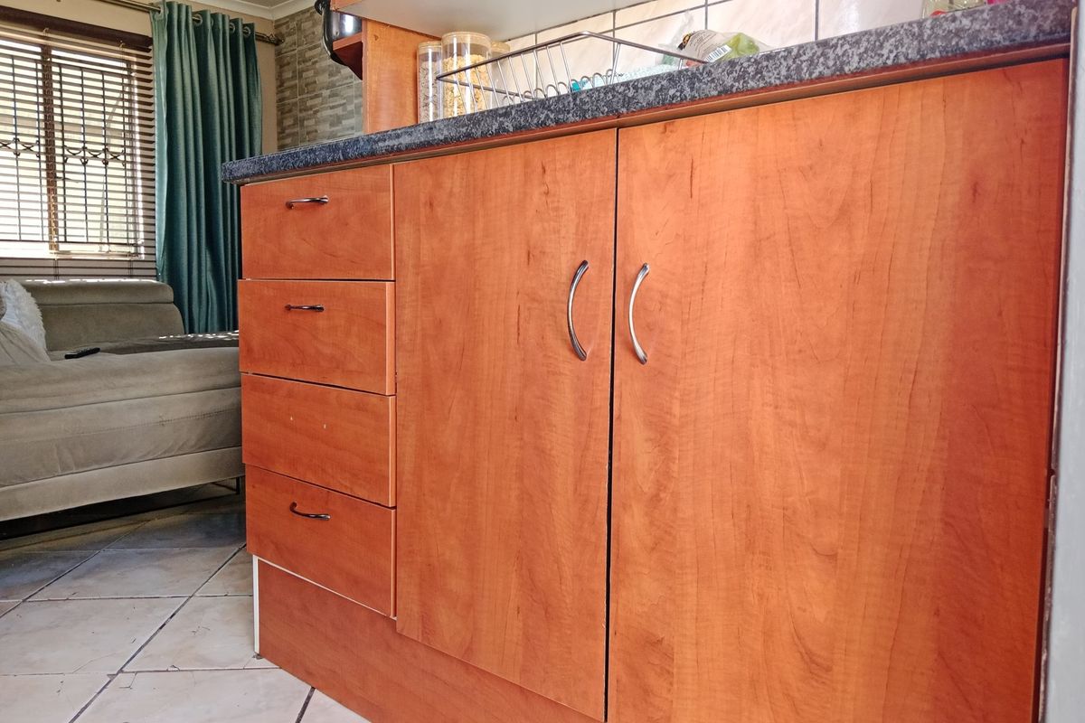 A close-up view of kitchen cabinetry featuring wood-look laminate doors, granite countertops, and a tiled backsplash in an open-plan living area.