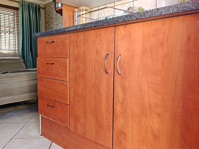 A close-up view of kitchen cabinetry featuring wood-look laminate doors, granite countertops, and a tiled backsplash in an open-plan living area.