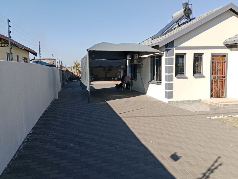 Front exterior view featuring a paved driveway, carport, solar water heater, and secure boundary wall with electric fencing.