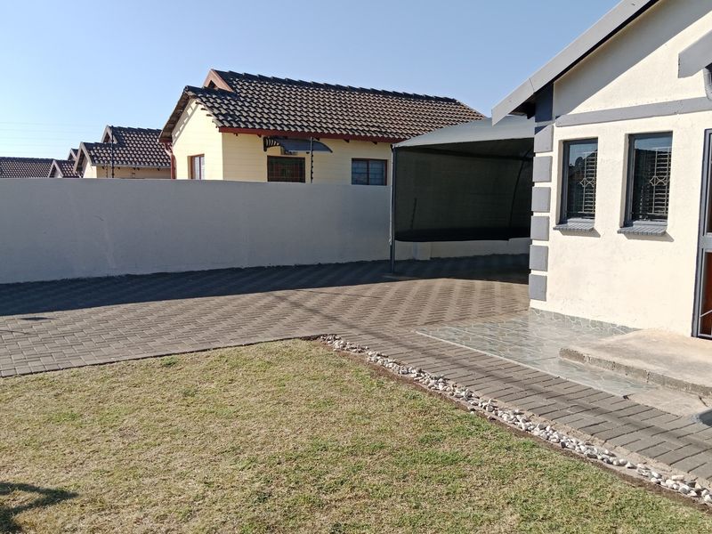 Front exterior view featuring a paved driveway, a covered carport, and a secure boundary wall with a well-maintained lawn area.