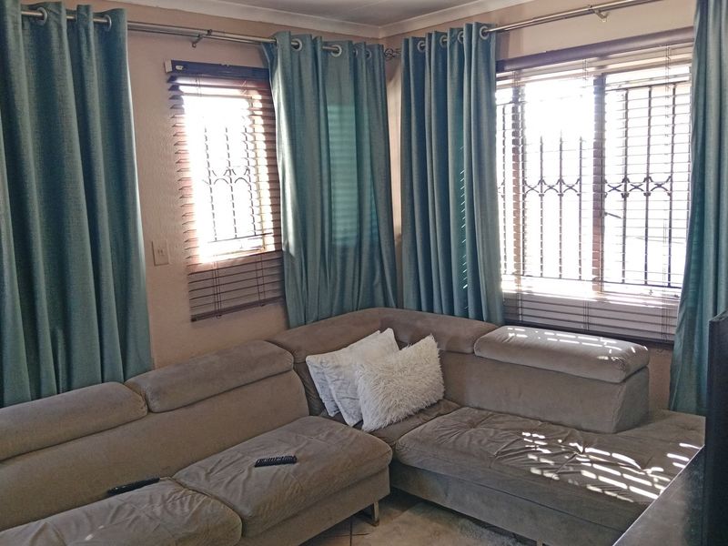 A living room area featuring corner windows with security bars, venetian blinds, and curtain rods.