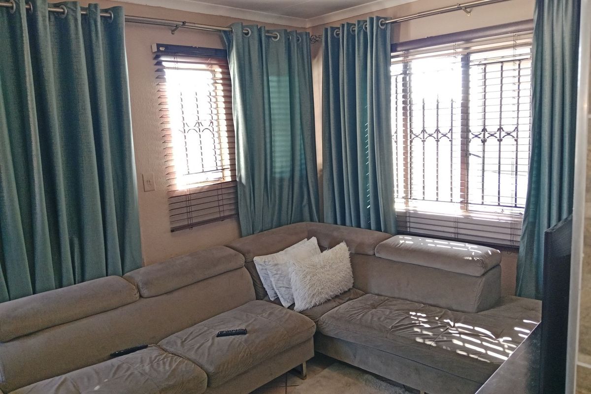 A living room area featuring corner windows with security bars, venetian blinds, and curtain rods.