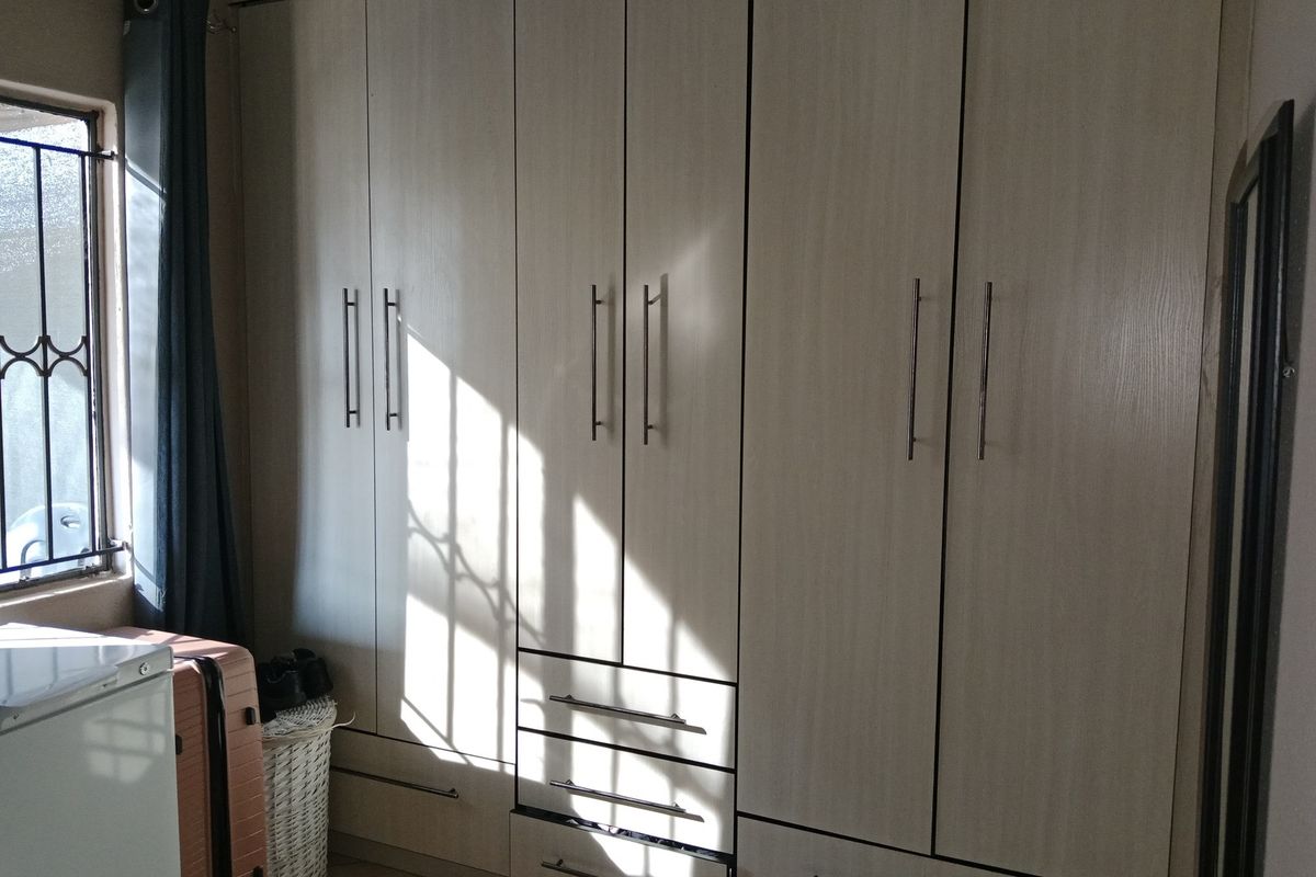 A bedroom featuring light-toned built-in cupboards with modern handles and a window fitted with security bars.