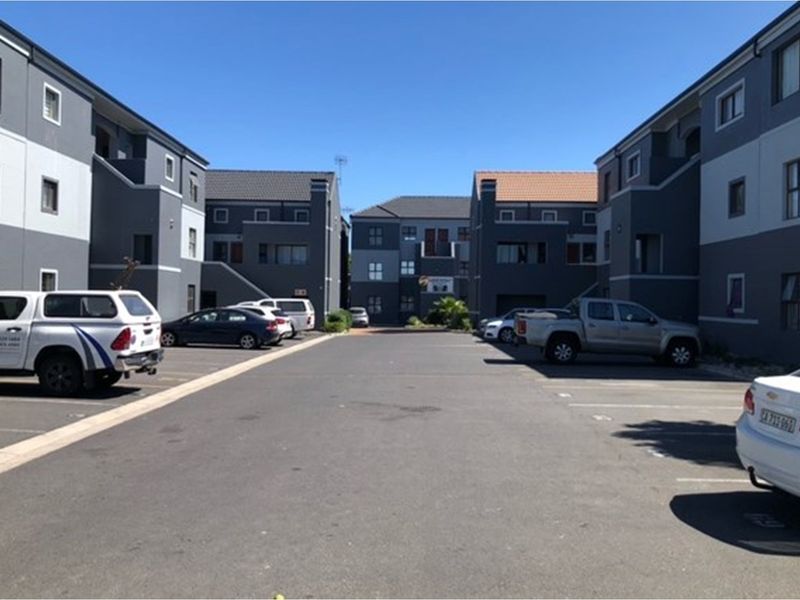 Exterior view of an apartment complex courtyard featuring paved parking areas and multi-story residential buildings with modern grey and white facades.