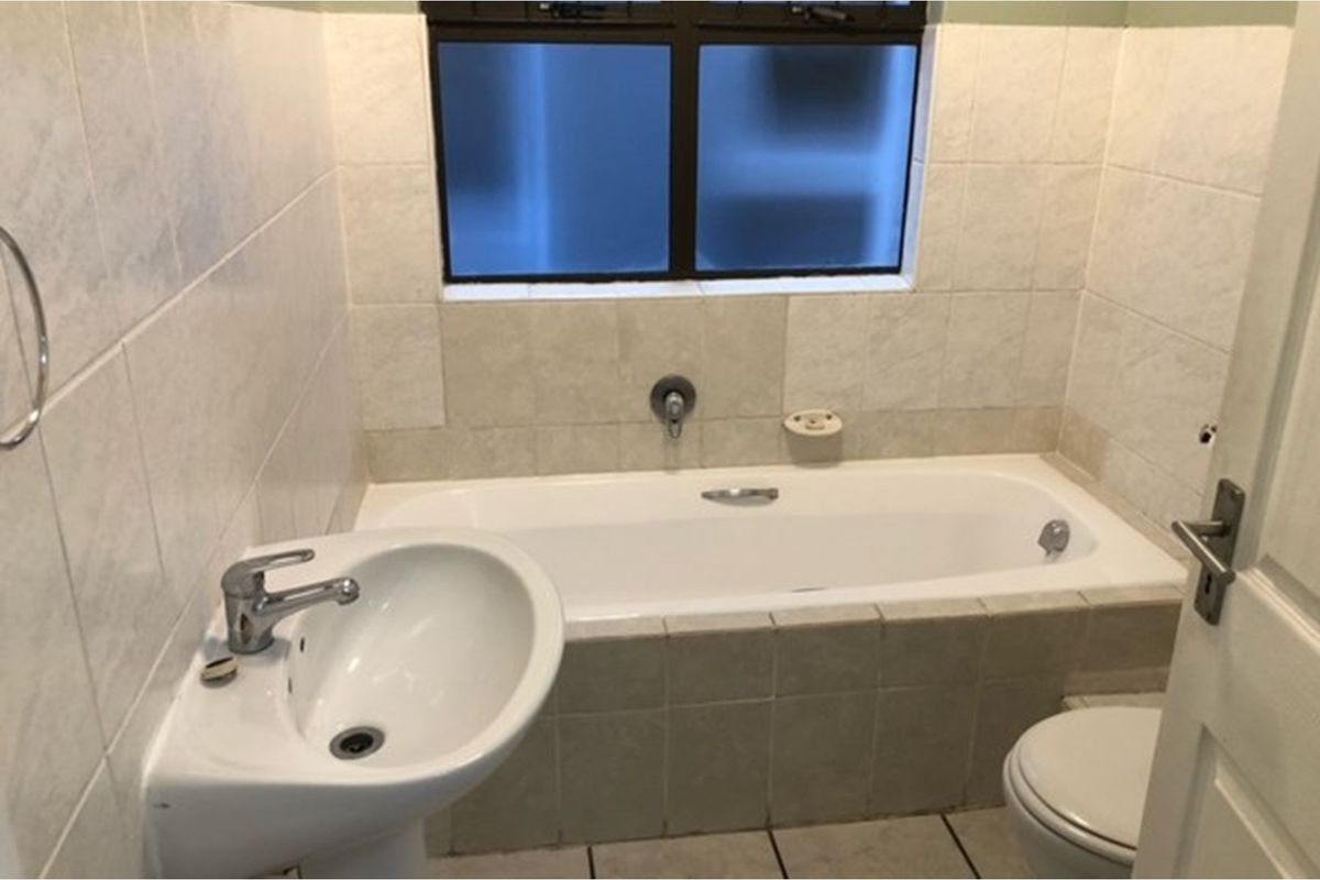 A functional bathroom featuring a built-in bathtub, pedestal basin, and toilet with neutral wall and floor tiling.