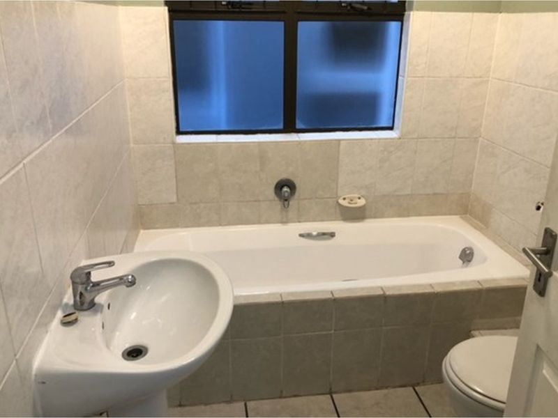 A functional bathroom featuring a built-in bathtub, pedestal basin, and toilet with neutral wall and floor tiling.