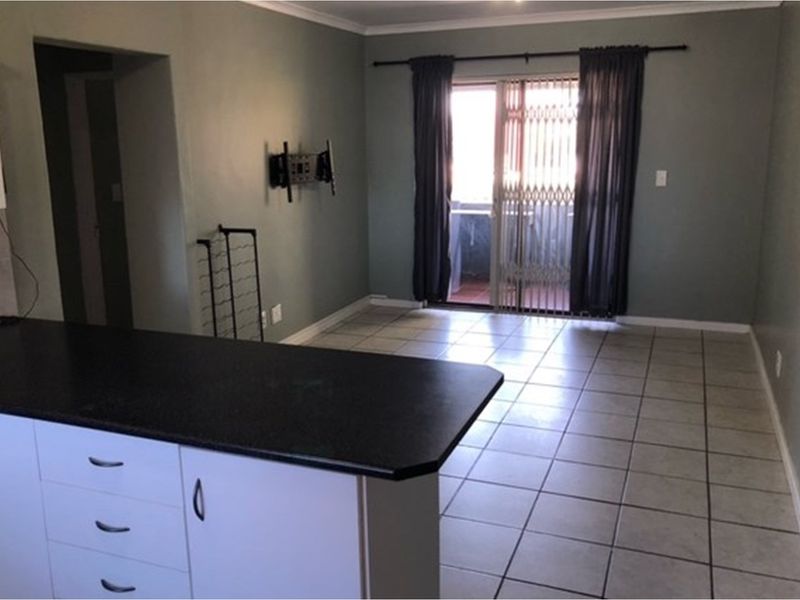 Open plan living area featuring tiled flooring and a kitchen breakfast bar, with direct access to a balcony through sliding glass doors.